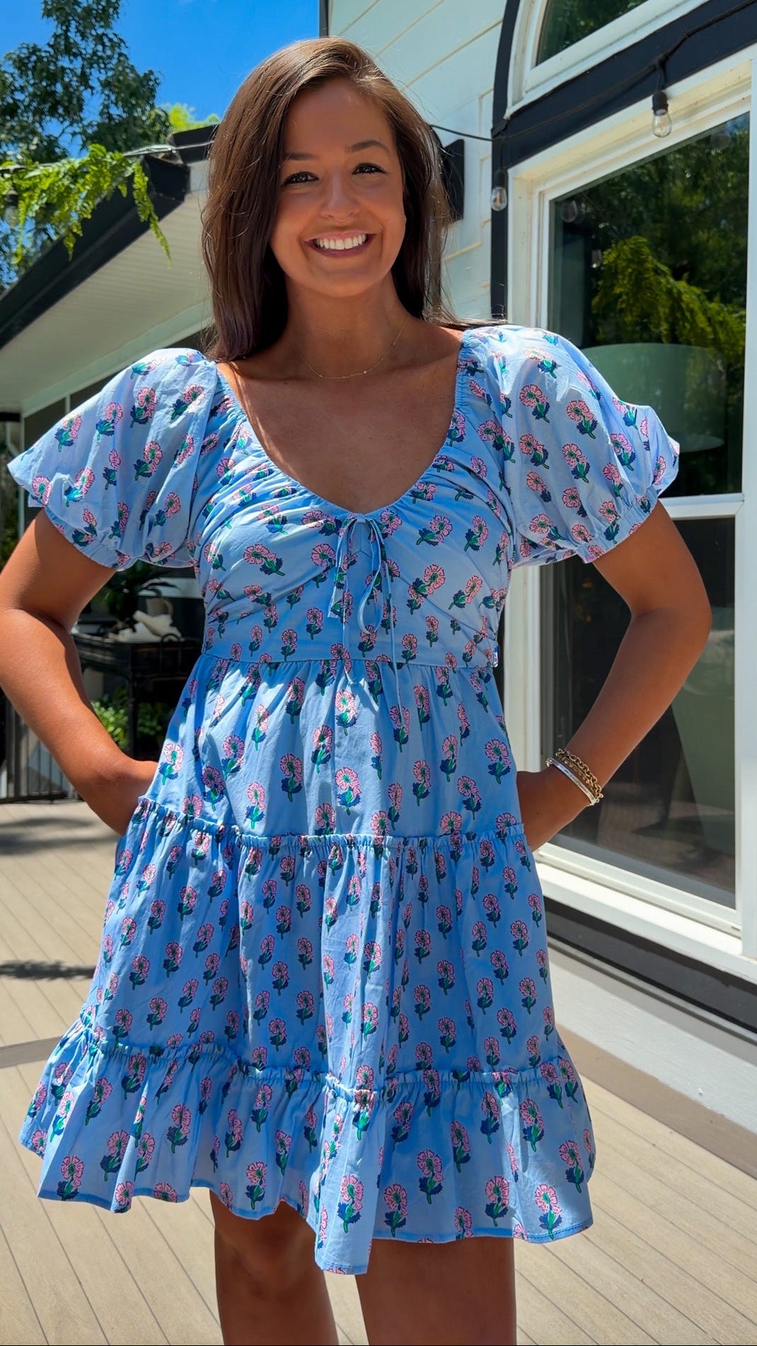Woman wearing a blue dress with floral pattern standing outdoors.