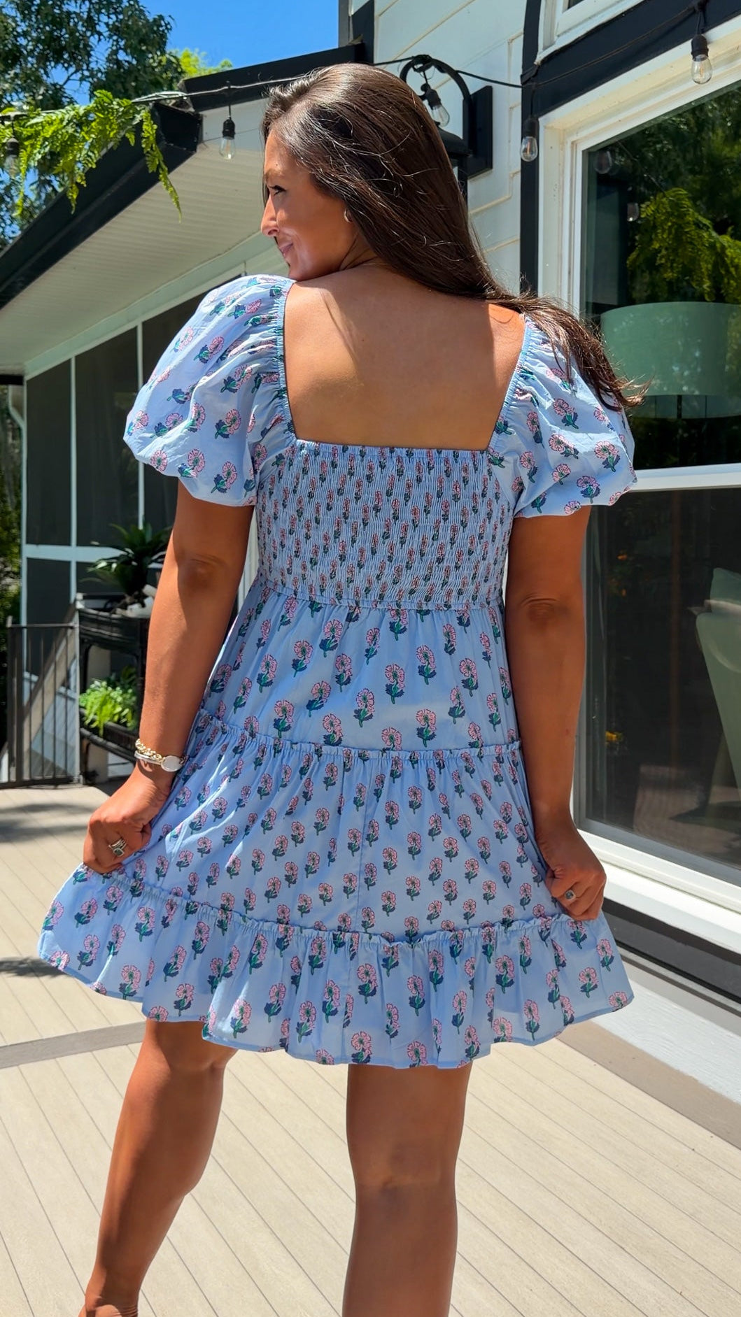 Woman wearing a blue floral dress standing on a wooden deck.