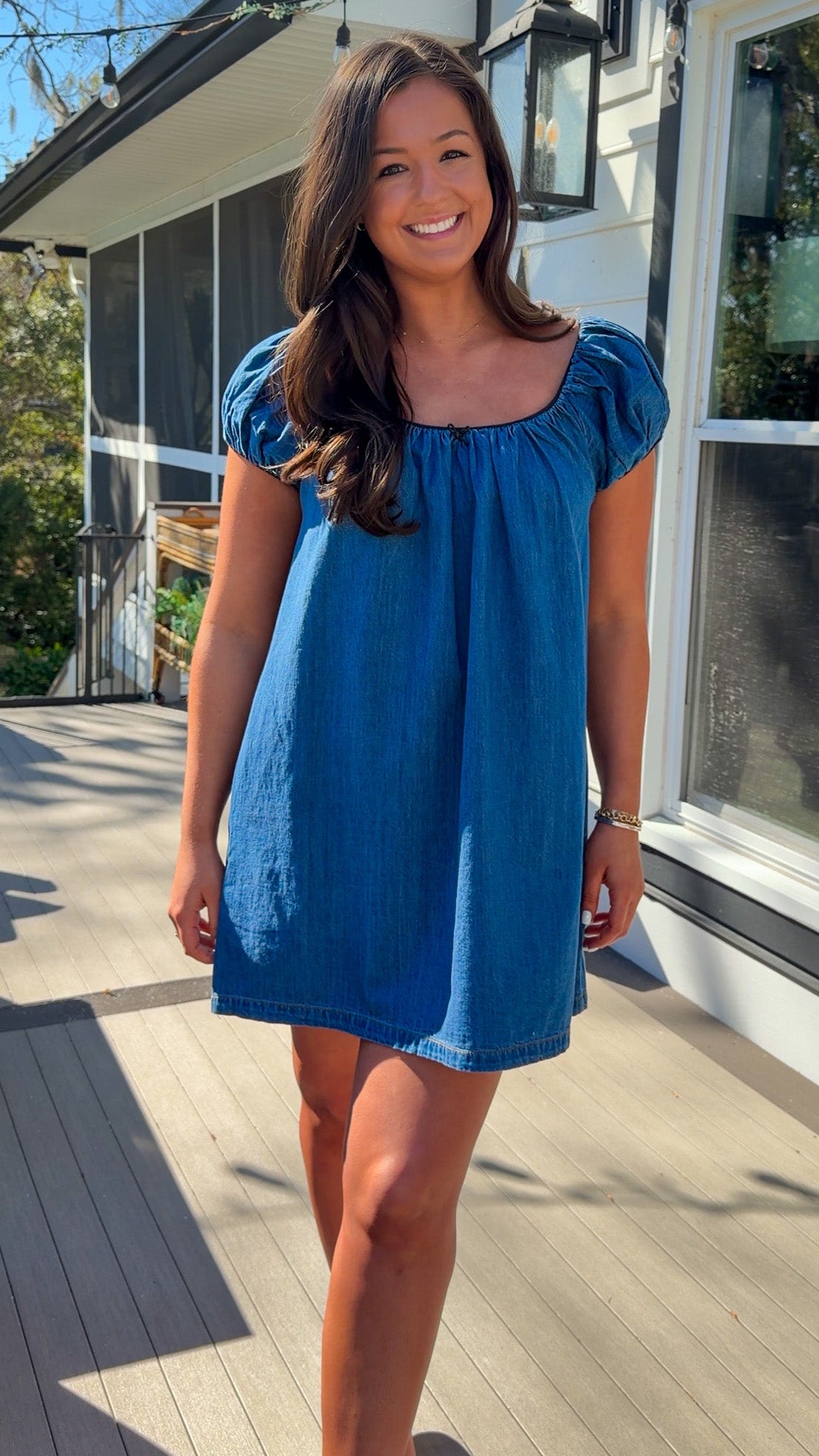 Blue denim mini dress with scoop neckline, short puff sleeves, and relaxed babydoll fit, worn outdoors in natural light.