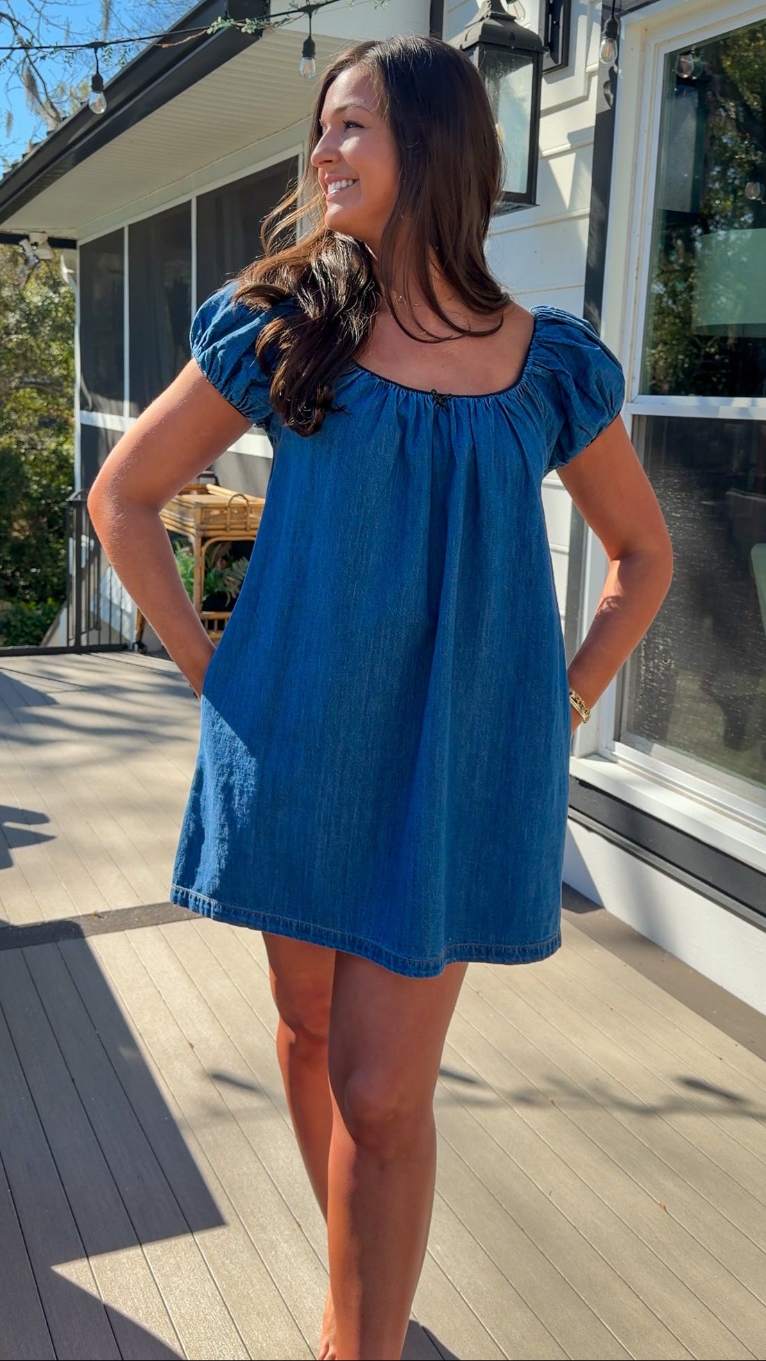 Blue denim mini dress with scoop neckline, short puff sleeves, and relaxed babydoll fit, worn outdoors in natural light.