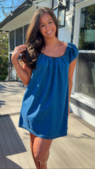 Blue denim mini dress with scoop neckline, short puff sleeves, and relaxed babydoll fit, worn outdoors in natural light.