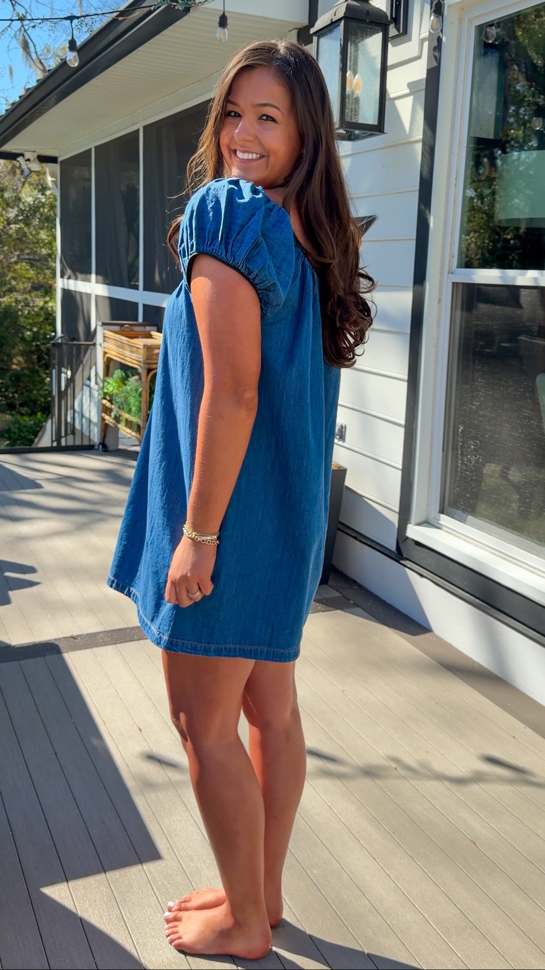 Blue denim mini dress with scoop neckline, short puff sleeves, and relaxed babydoll fit, worn outdoors in natural light.