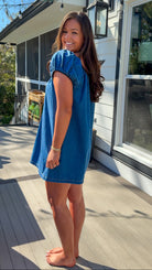 Blue denim mini dress with scoop neckline, short puff sleeves, and relaxed babydoll fit, worn outdoors in natural light.
