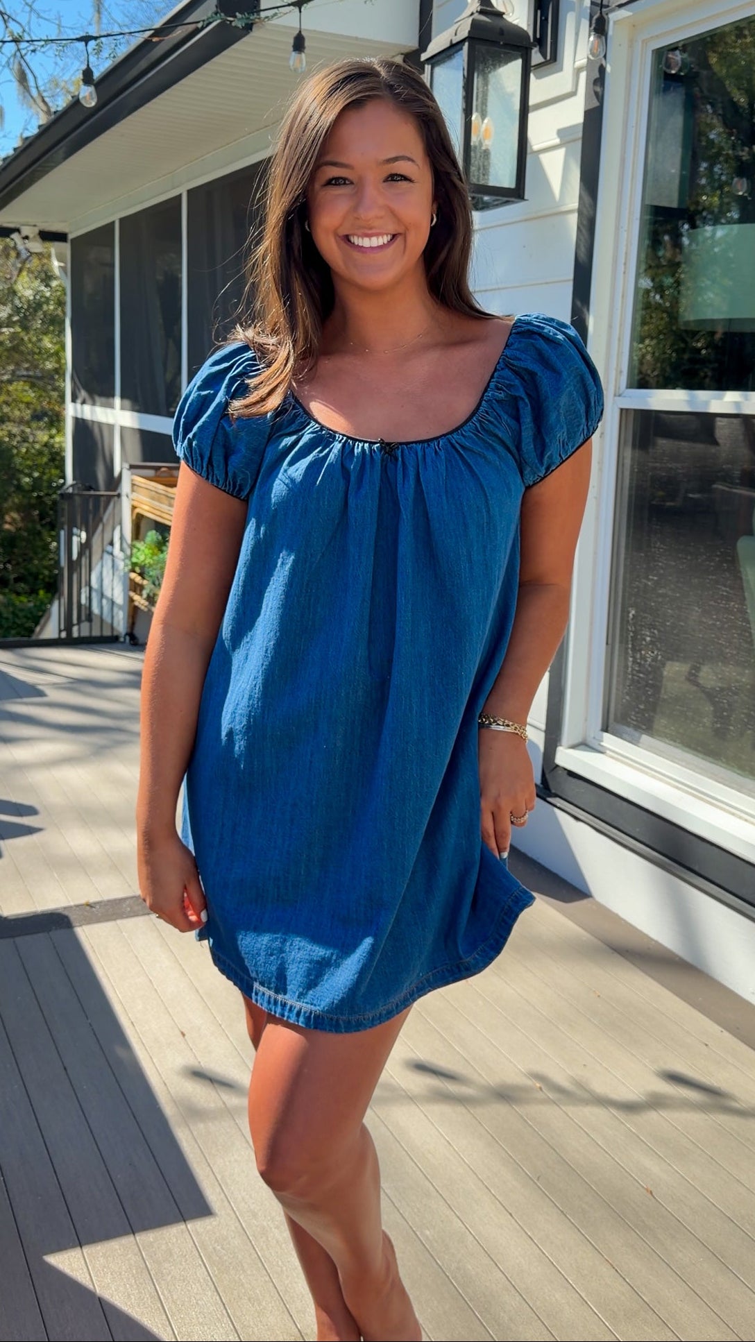 Blue denim mini dress with scoop neckline, short puff sleeves, and relaxed babydoll fit, worn outdoors in natural light.