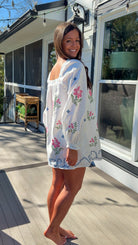 White embroidered mini dress with square neckline, long sleeves, and colorful floral embroidery, worn outdoors in natural light.