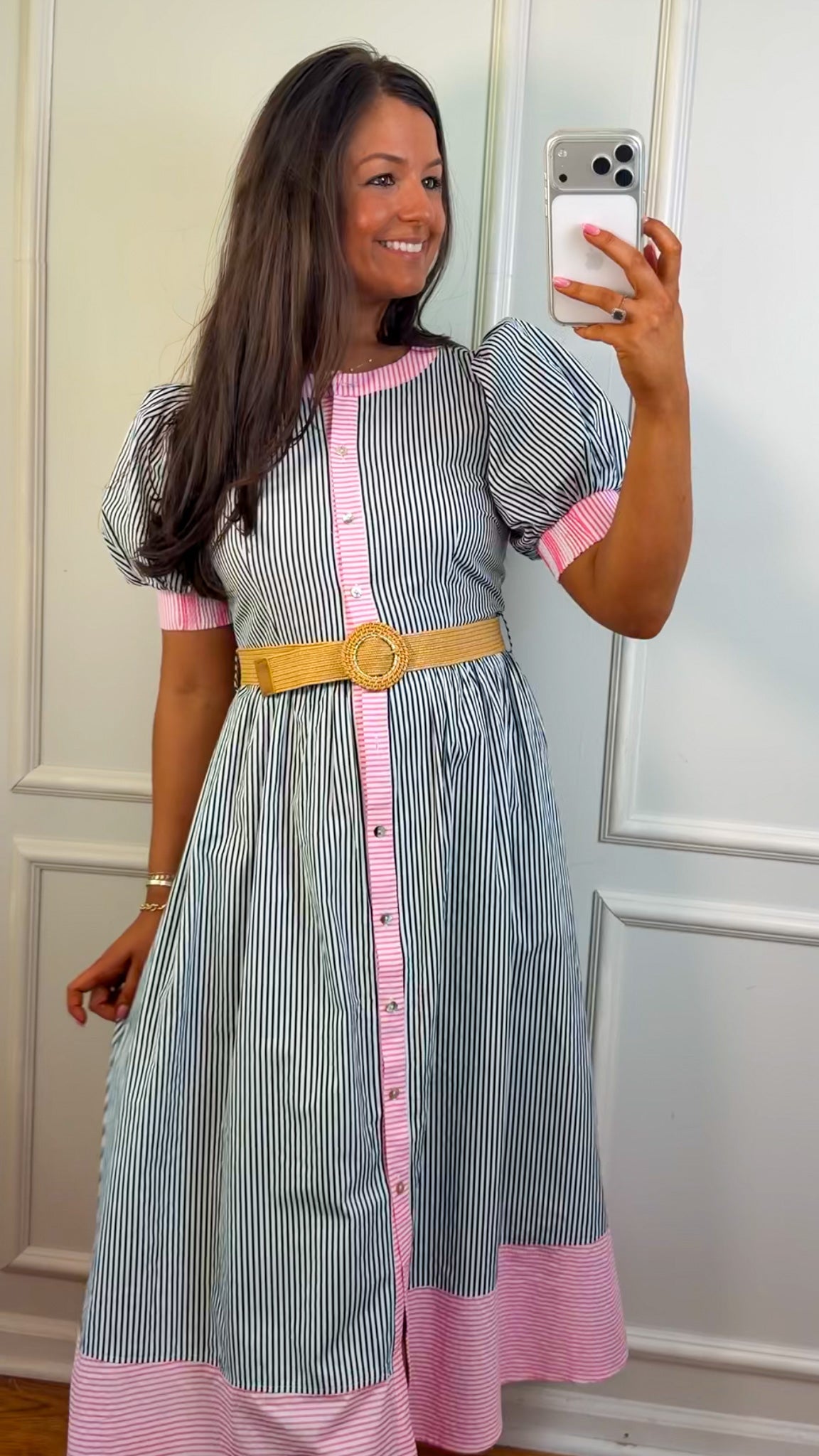 Woman taking a mirror selfie wearing a striped dress with pink accents and a yellow belt.