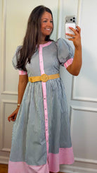 Woman taking a mirror selfie wearing a striped dress with pink accents and a yellow belt.