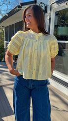 Woman wearing a yellow blouse with floral patterns and blue jeans standing outdoors.