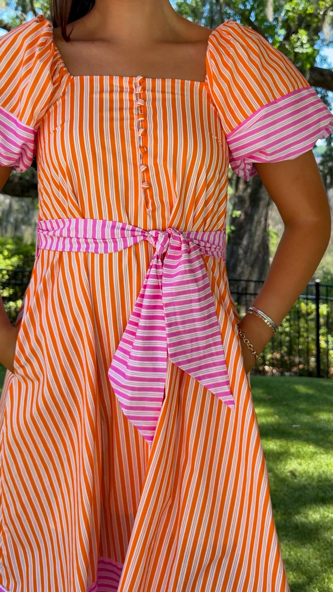 Person wearing an orange and pink striped dress with a blurred outdoor background