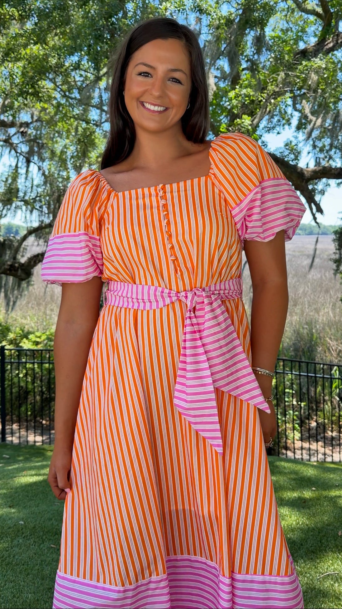 Woman wearing an orange and pink striped dress with a garden background