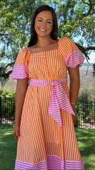 Woman wearing an orange and pink striped dress with a garden background