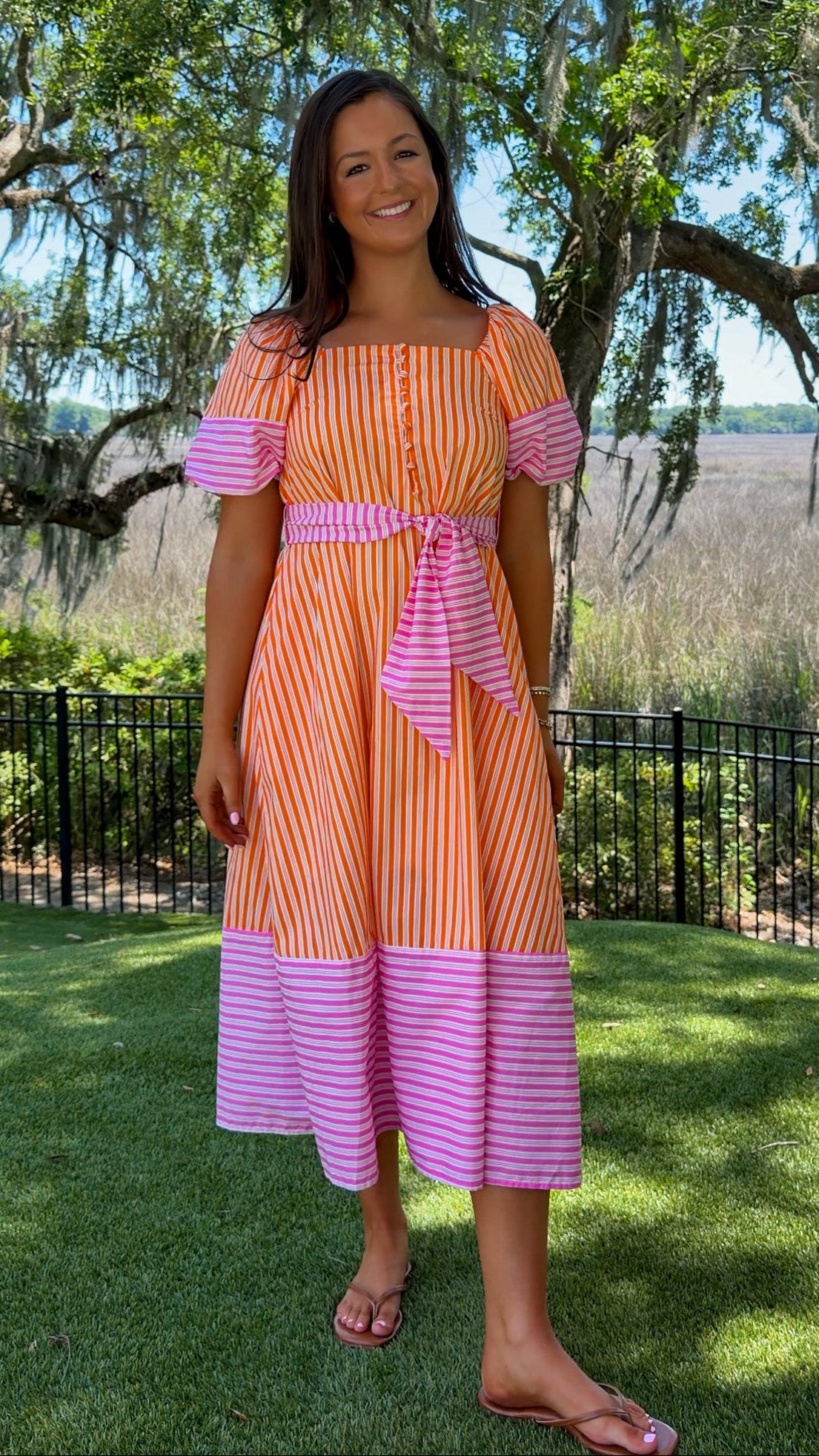 Woman wearing a striped dress standing outdoors with trees and grass in the background