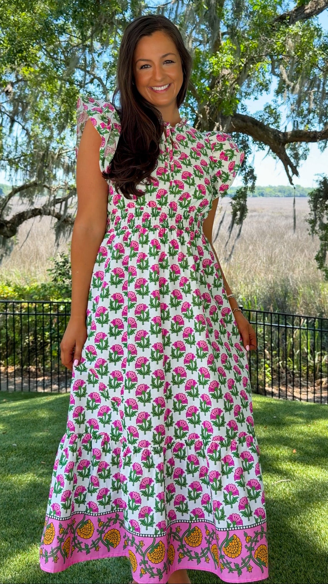 Woman wearing a floral dress standing outdoors with trees and grass in the background
