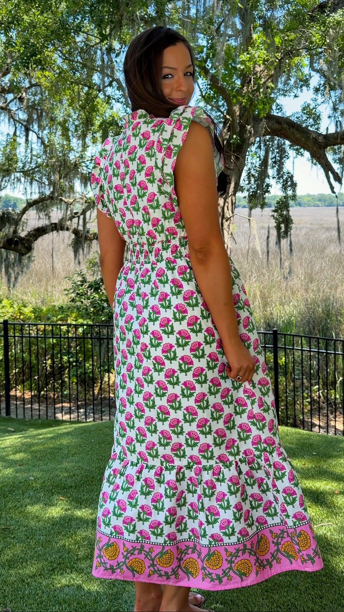 Woman in a floral dress standing outdoors with trees and grass in the background