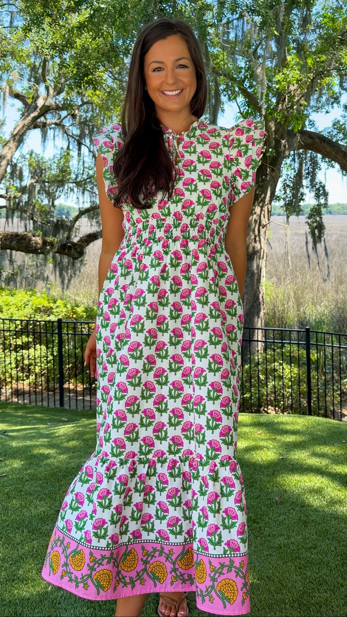 Woman wearing a floral dress standing outdoors with trees and grass in the background