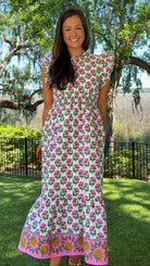 Woman wearing a floral dress standing outdoors with trees and grass in the background