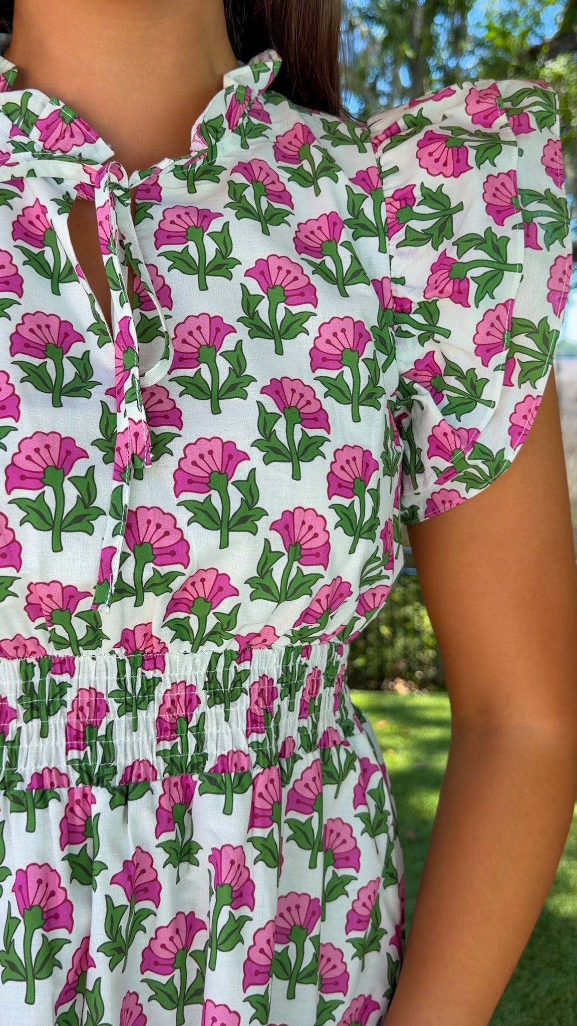 Person wearing a floral dress with pink and green flowers in an outdoor setting