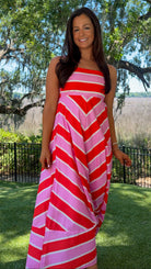 Woman wearing a red and pink striped dress standing outdoors with trees and grass in the background