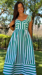 Woman wearing a green and white striped dress standing outdoors with trees and grass in the background