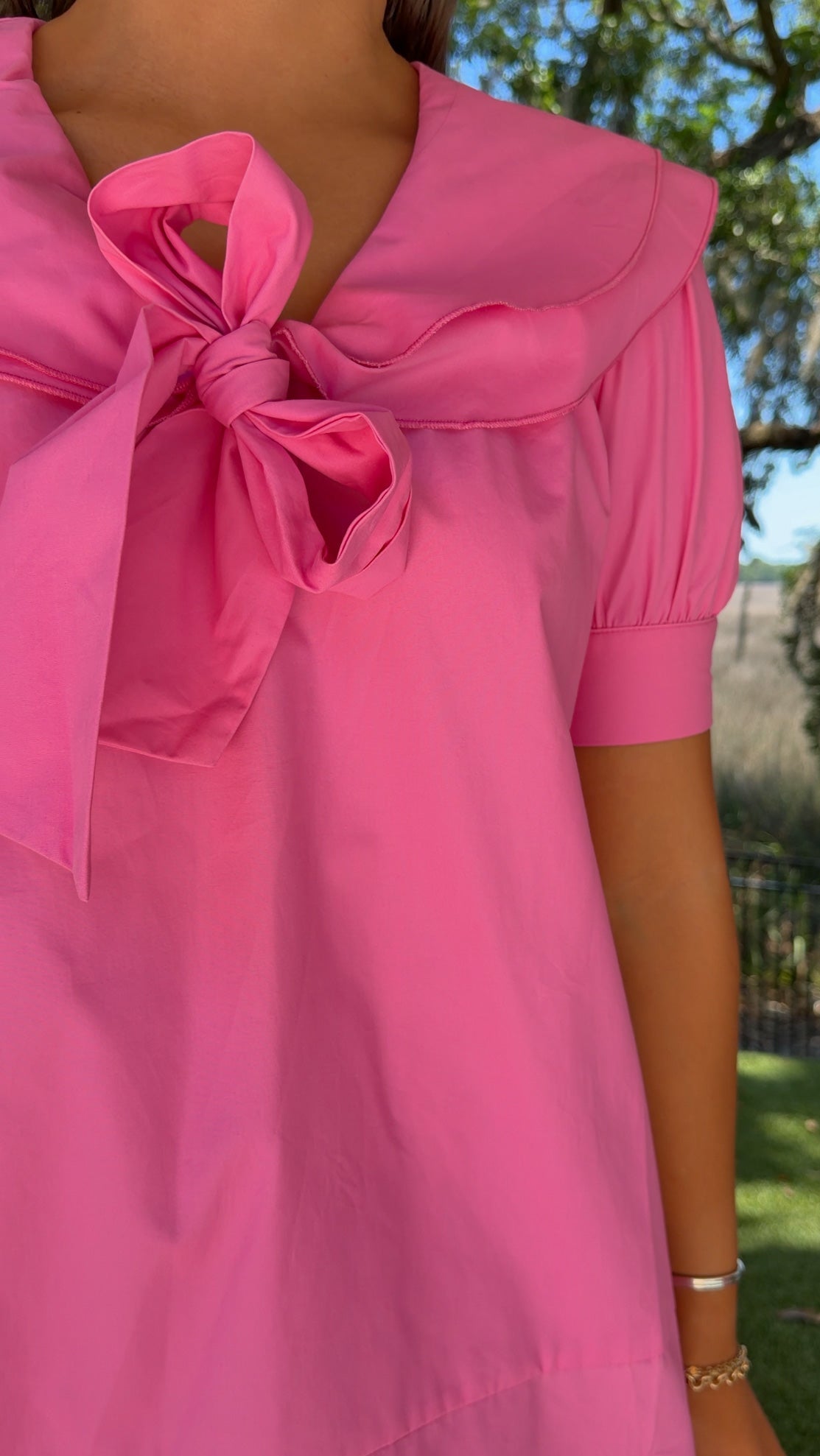 Close-up of a pink dress with a bow detail, worn outdoors.