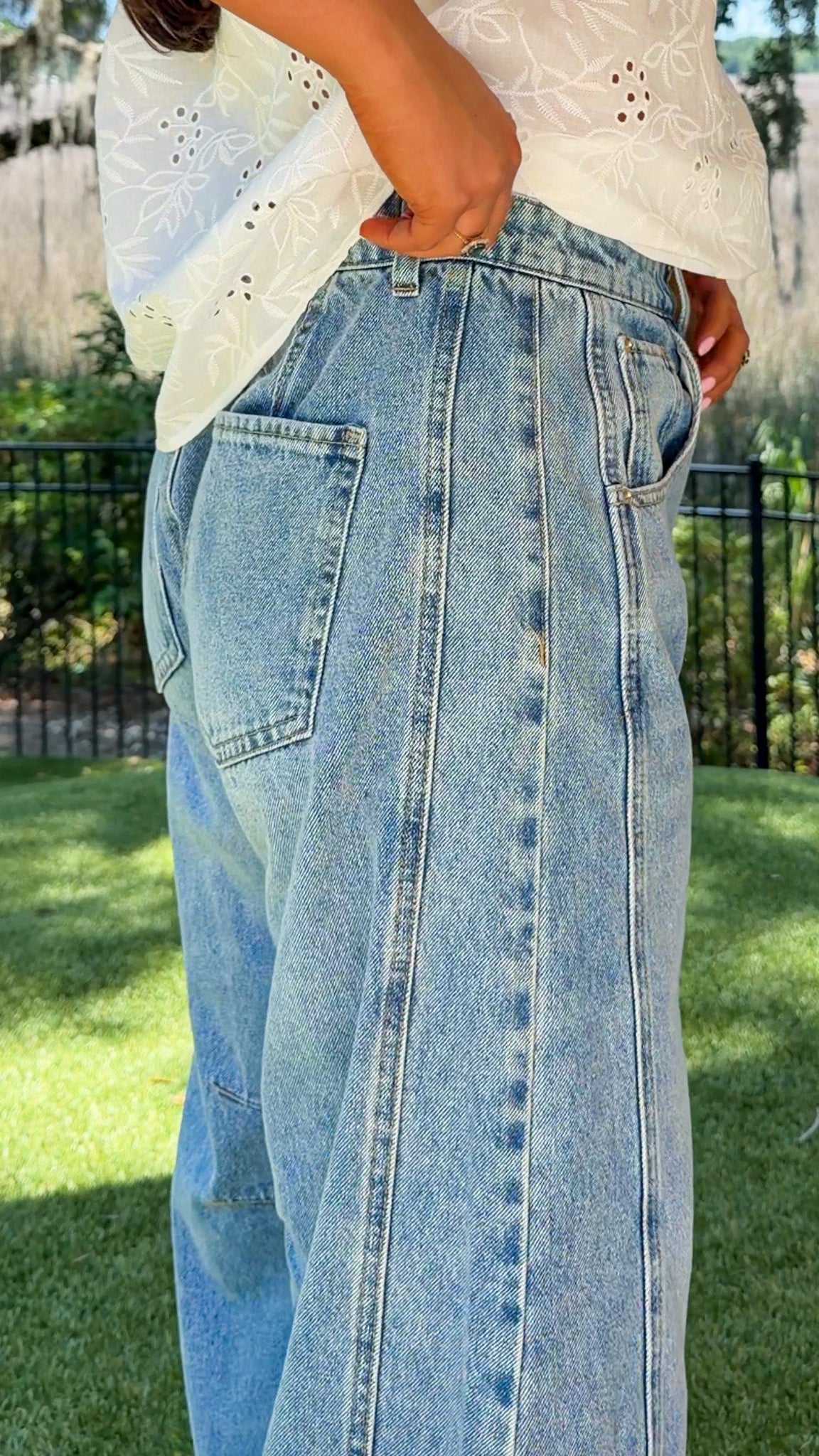 Person wearing light blue jeans and a white top outdoors on a sunny day.
