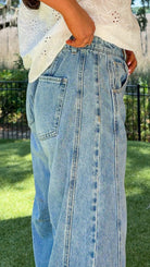 Person wearing light blue jeans and a white top outdoors on a sunny day.
