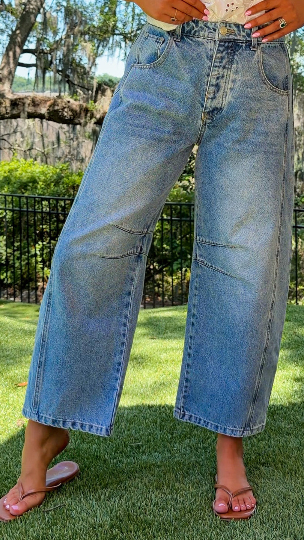 Person wearing light blue jeans and a white top standing on grass with trees in the background