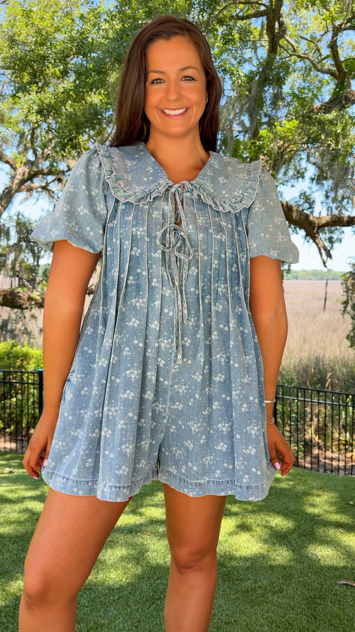 Woman wearing a blue floral dress standing outdoors with trees and grass in the background