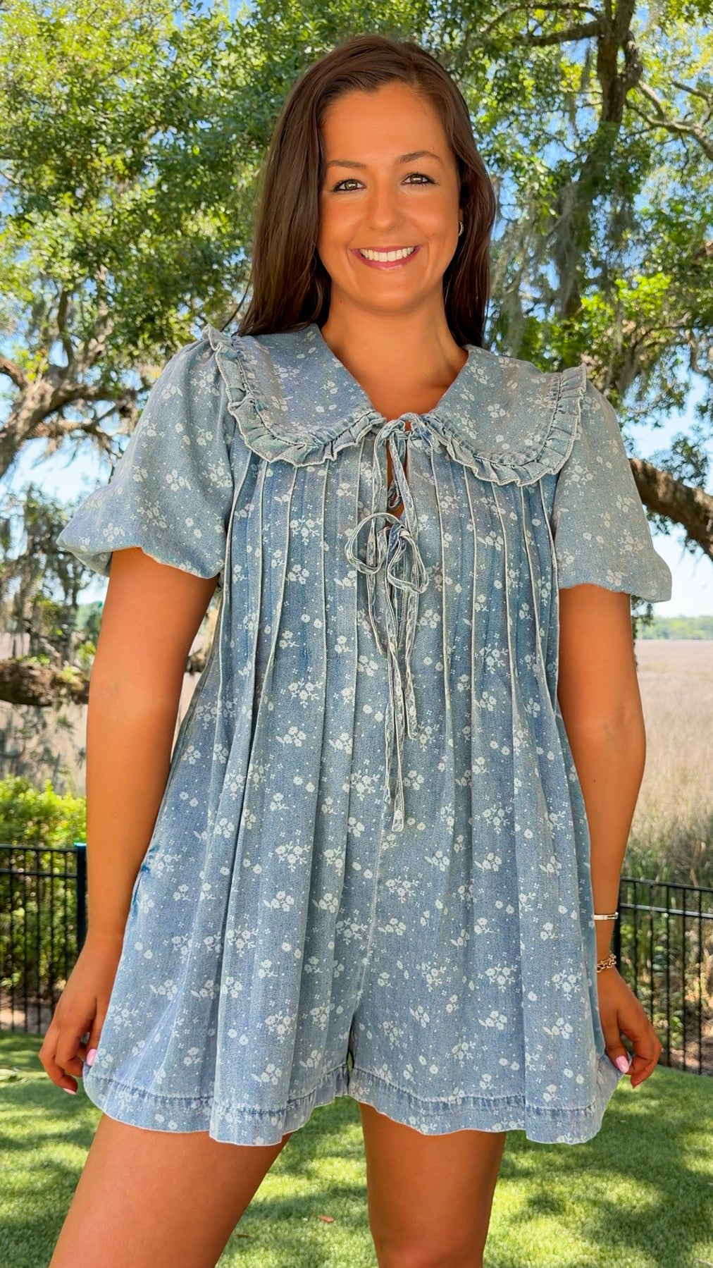 Woman wearing a blue floral dress standing outdoors with trees and grass in the background
