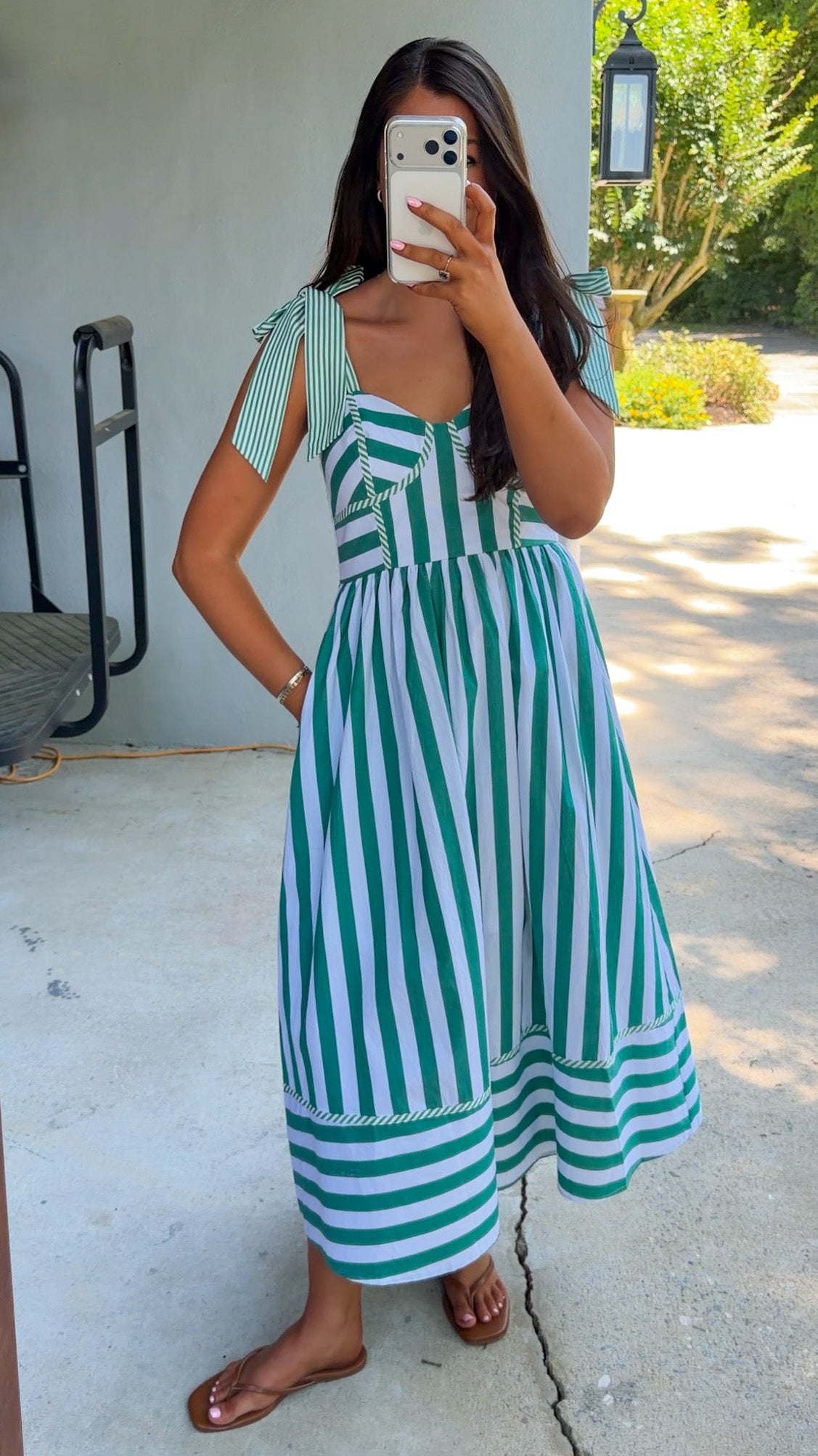 Woman wearing a green and white striped dress taking a mirror selfie outdoors.