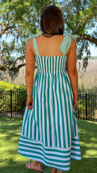 Woman wearing a green and white striped dress standing in a park-like setting with trees and grass.
