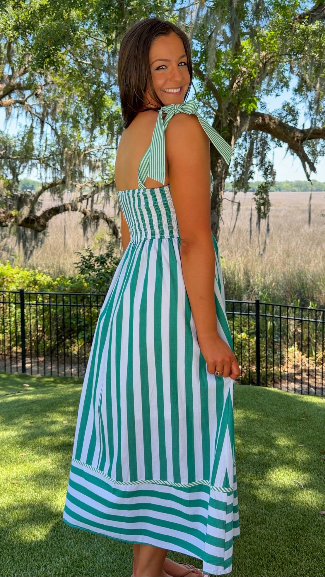 Woman wearing a green and white striped dress standing outdoors with trees and grass in the background