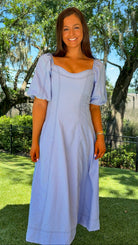 Woman in a light blue dress standing outdoors with trees and grass in the background