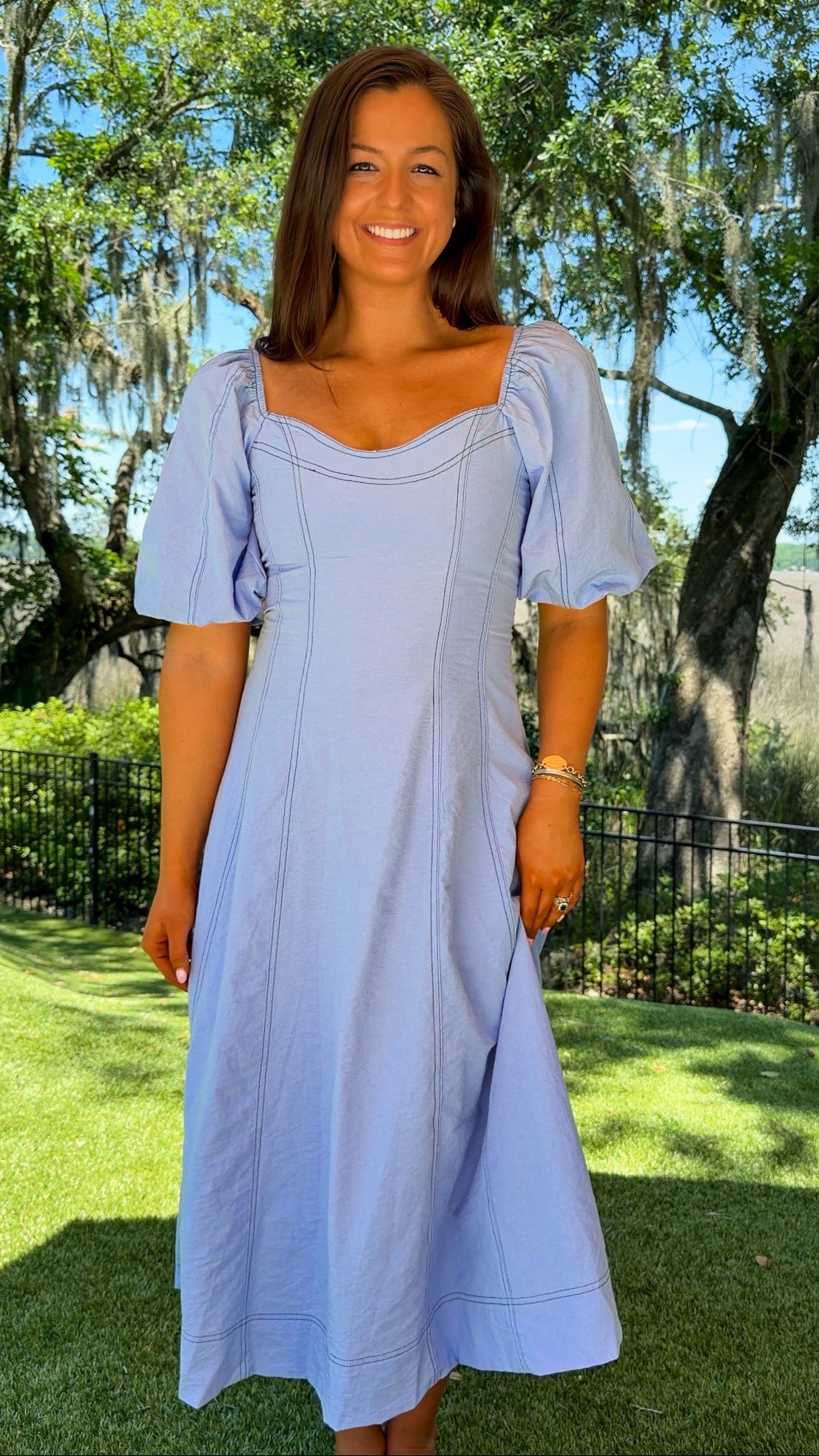 Woman in a light blue dress standing outdoors with trees and grass in the background