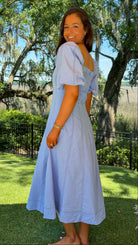 Woman in a light blue dress standing outdoors with trees and grass in the background