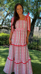 Woman in a red and white dress standing outdoors with trees and grass in the background