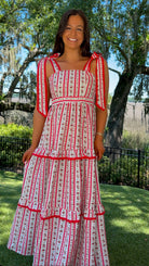 Woman wearing a red and white patterned dress standing outdoors with trees and grass in the background