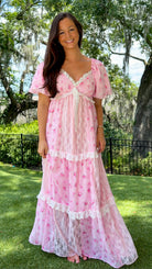 Pink floral maxi dress with delicate rose print, lace-trimmed V-neckline, puff short sleeves, empire waist, smocked back, and tiered skirt with lace panel details