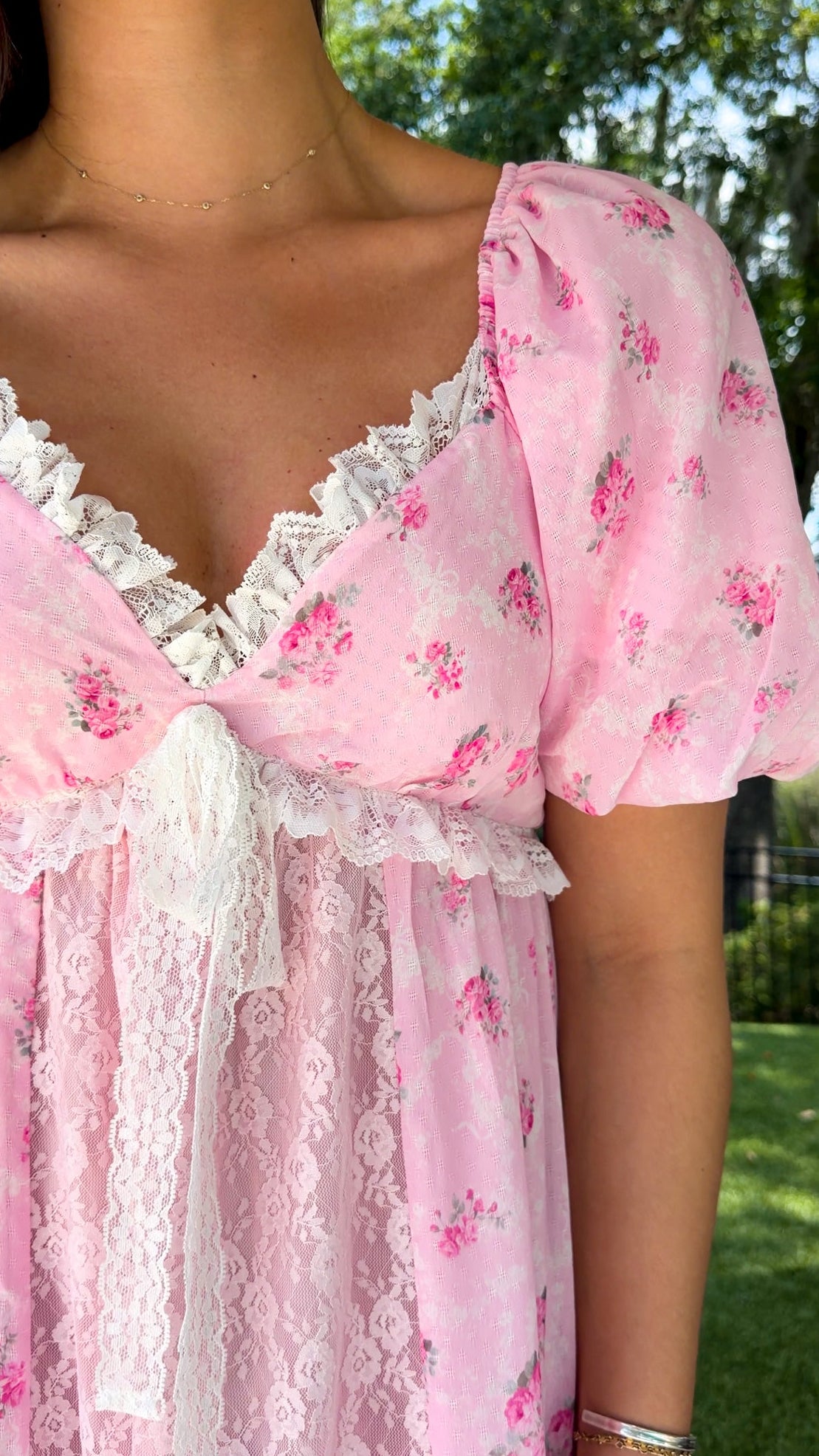 Pink floral maxi dress with delicate rose print, lace-trimmed V-neckline, puff short sleeves, empire waist, smocked back, and tiered skirt with lace panel details