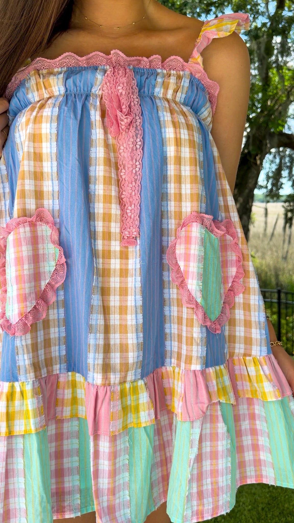 Pastel patchwork mini dress featuring mixed check and stripe prints in pink, blue, yellow, and mint with ruffle straps, heart-shaped front pockets, pink lace trim, and a relaxed babydoll silhouette.