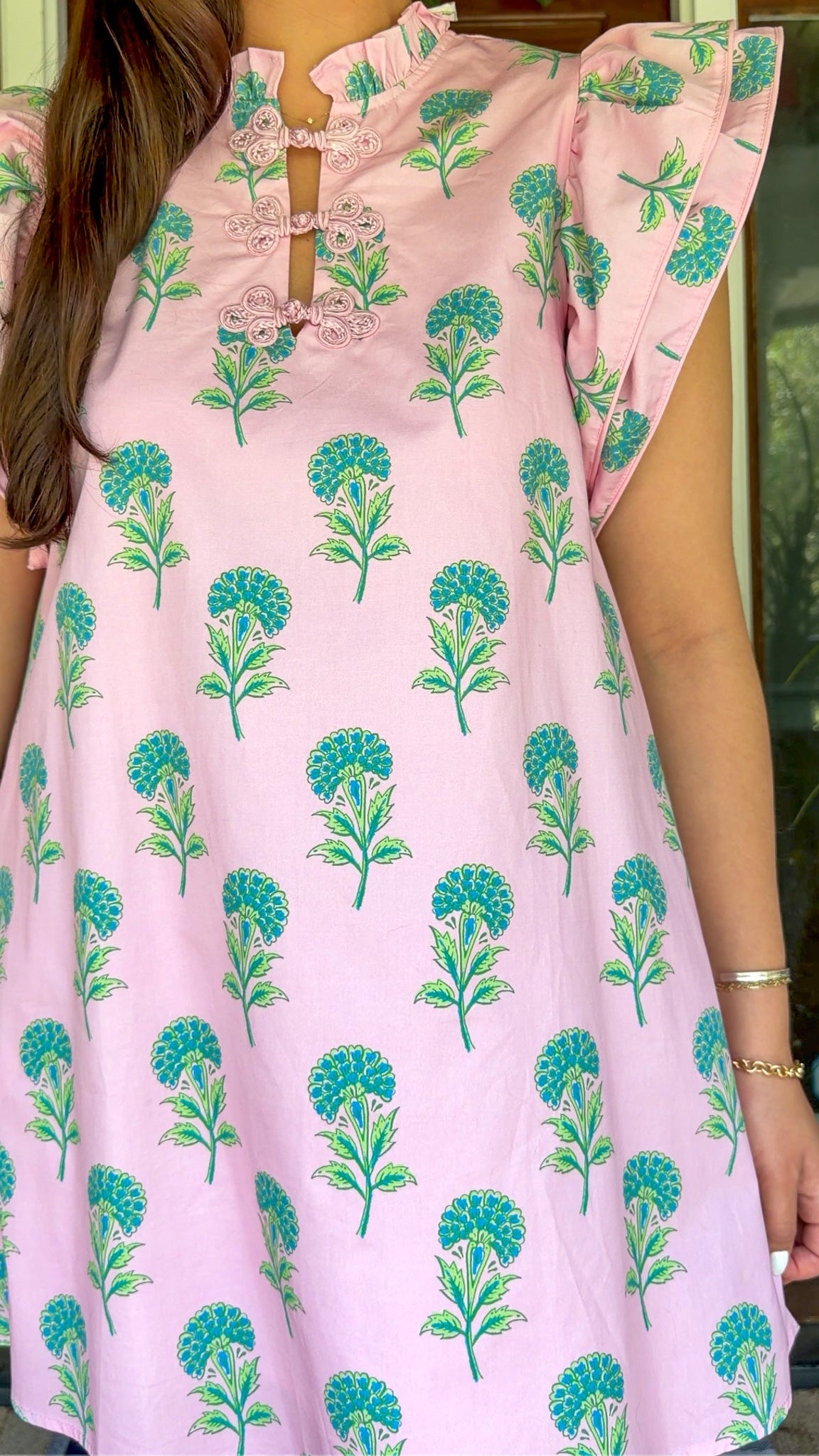 Pink and green floral mini dress with flutter sleeves, a ruffled stand neckline, decorative frog button closures, and a relaxed shift silhouette.