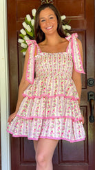 Pastel pink floral tiered mini dress with a smocked bodice, adjustable shoulder tie straps, lace trim detailing, and a flowy tiered skirt.