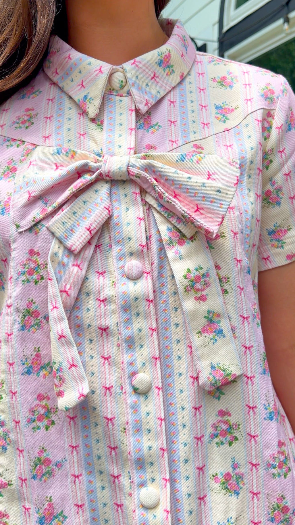 Light pink floral stripe mini dress with a collared neckline, front button closure, short sleeves, oversized bow detail, and relaxed A-line silhouette.