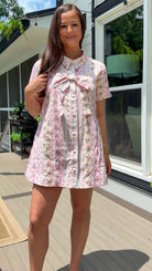Light pink floral stripe mini dress with a collared neckline, front button closure, short sleeves, oversized bow detail, and relaxed A-line silhouette.