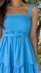 Blue midi dress featuring a square neckline, adjustable scalloped shoulder straps, scalloped trim at the empire waist and tiered skirt, a smocked back, and a flowing A-line silhouette.
