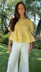 Butter yellow babydoll top featuring a round neckline, tiered shirring, short puff sleeves with adjustable tie cuffs, a ruffle-trimmed back, keyhole button closure, and a relaxed semi-cropped silhouette.