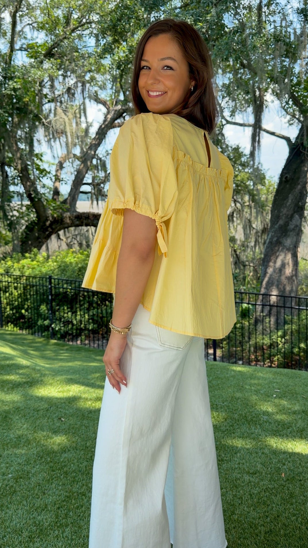 Butter yellow babydoll top featuring a round neckline, tiered shirring, short puff sleeves with adjustable tie cuffs, a ruffle-trimmed back, keyhole button closure, and a relaxed semi-cropped silhouette.