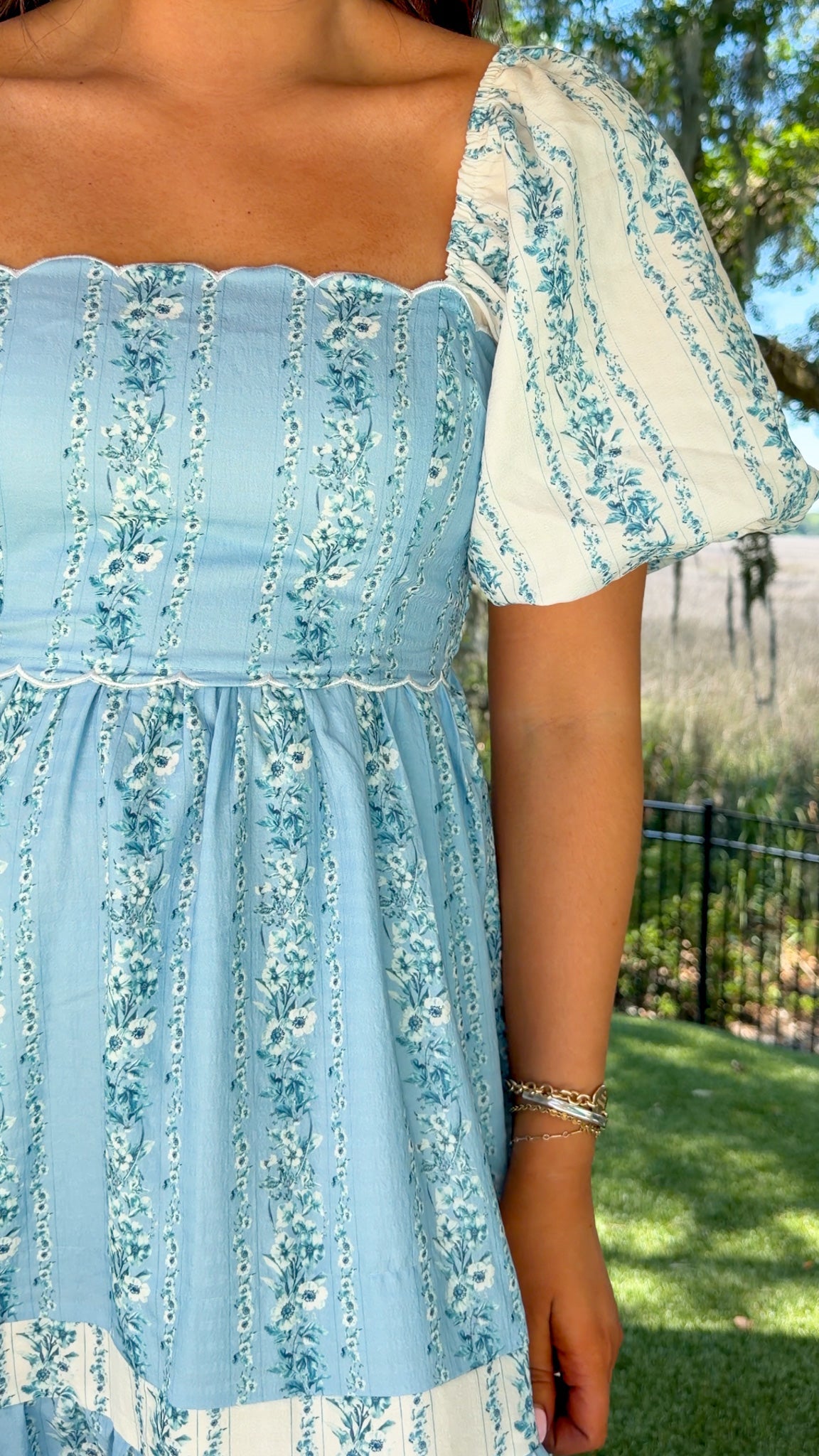 Person wearing a light blue floral dress with a blurred outdoor background