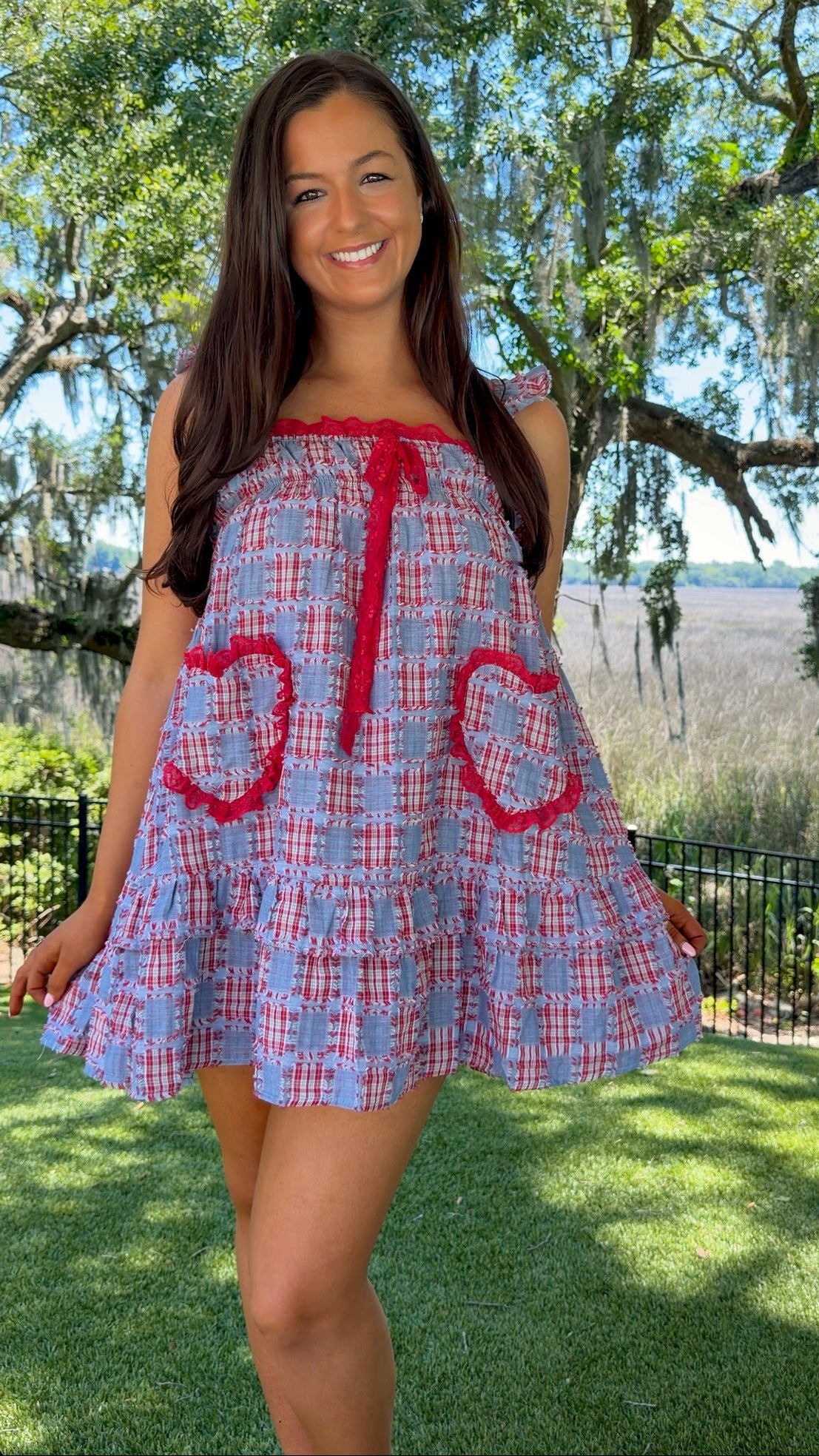 Woman wearing a blue and red checkered dress with heart designs outdoors.