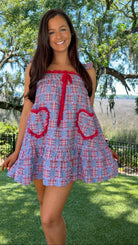 Woman wearing a blue and red checkered dress with heart designs outdoors.